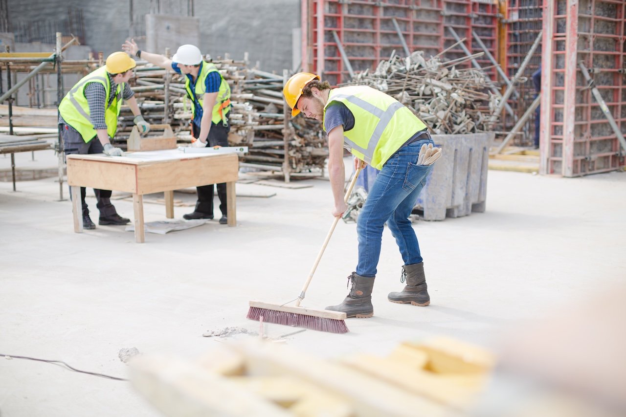 Construction worker sweeping debris at a construction site, maintaining cleanliness and safety during a building project.