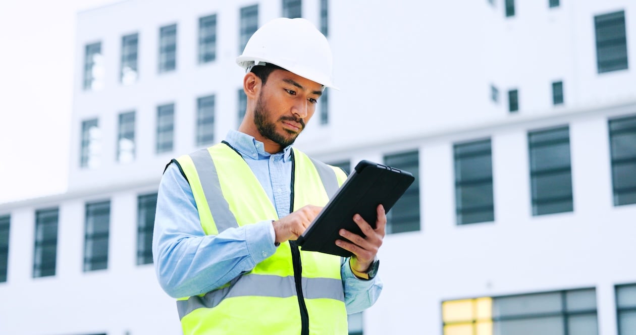 Male technician using a digital tablet to review project details while overseeing work at a job site, representing restoration project management and field documentation.