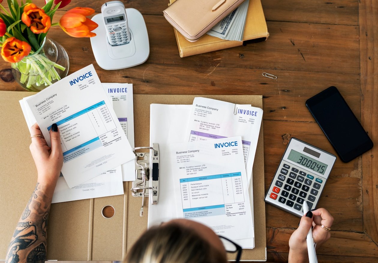Restoration office employee reviewing invoices, job files, and operational paperwork while managing payment workflows and administrative backlog at a busy desk.