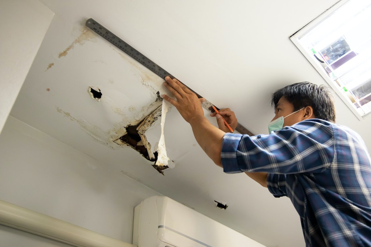 Worker fixing ceiling tiles caused by a water leak.