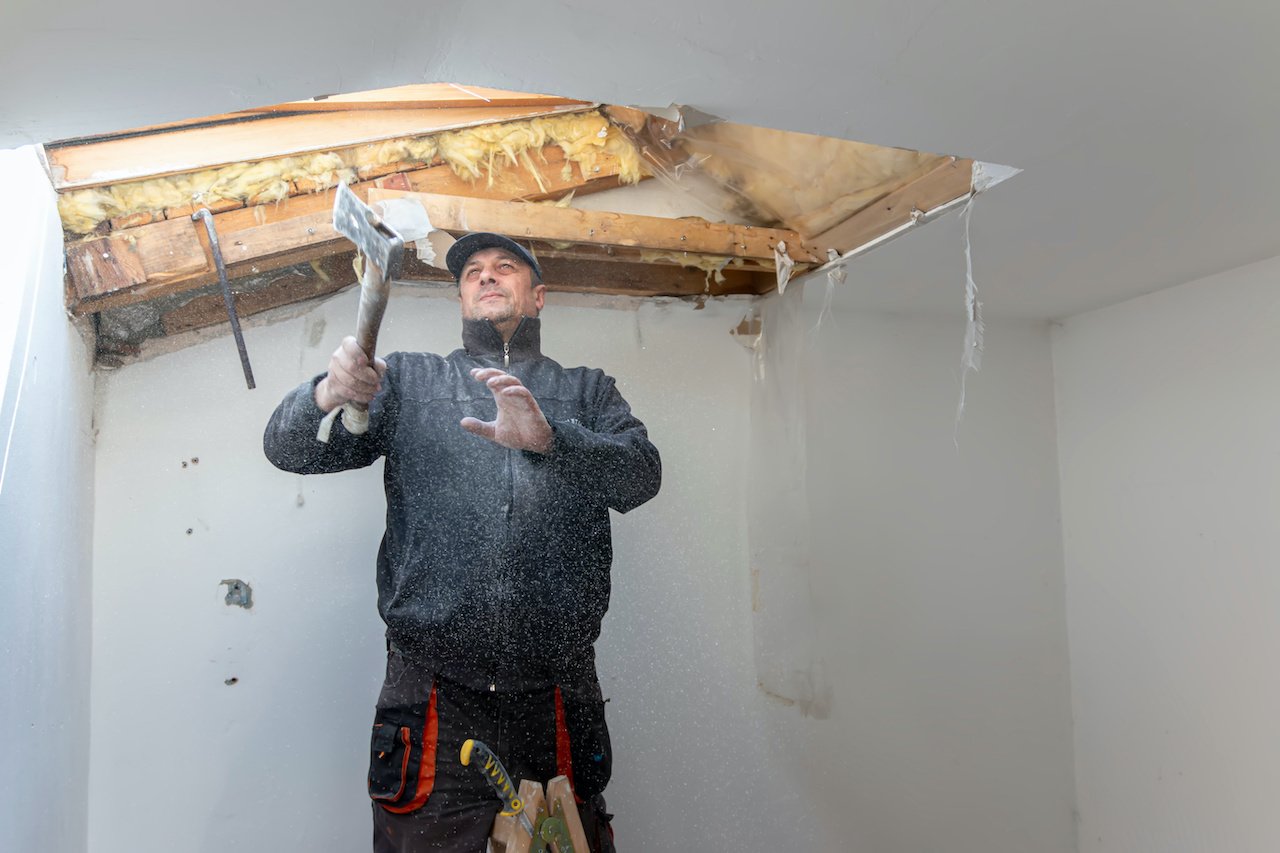 Man working on a damaged ceiling with axe. 
