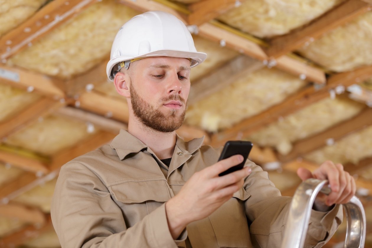 Restoration technician checking job details on a smartphone at a work site