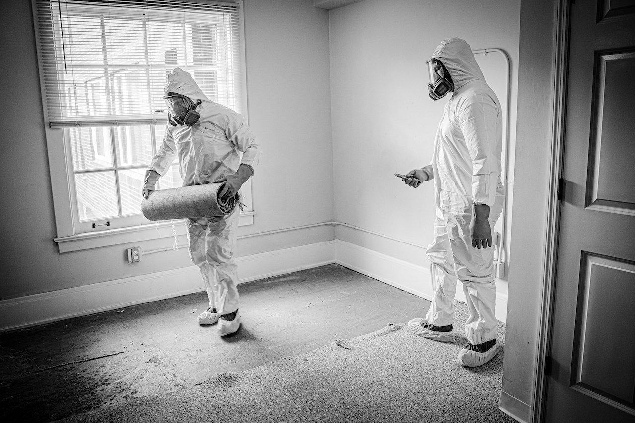 Two workers in protective gear removing carpet