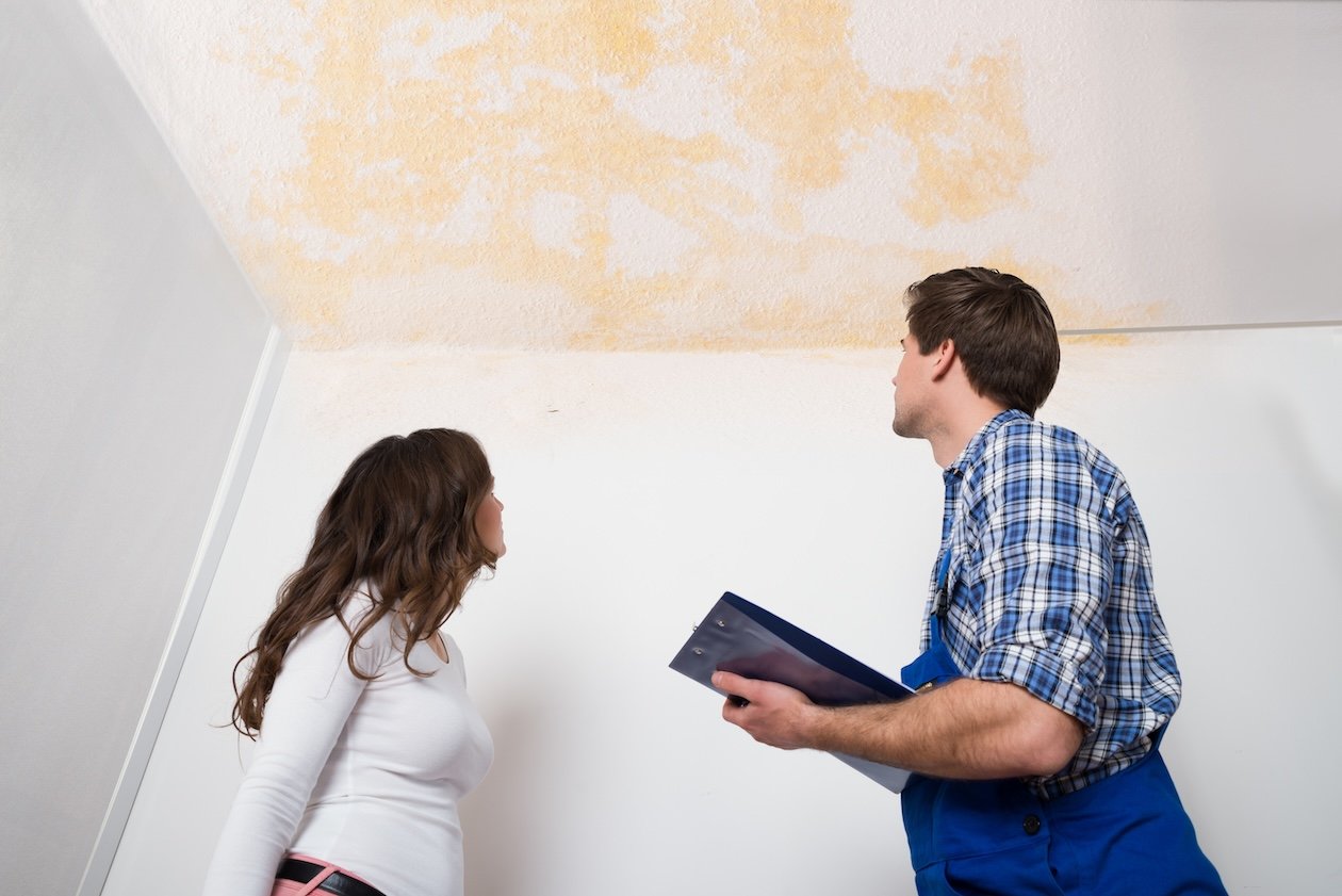 Technician documenting job intake details with a homeowner during an inspection inside a water-damaged house.